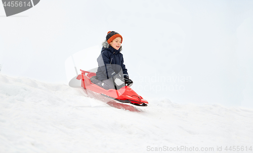 Image of happy boy sliding on sled down snow hill in winter