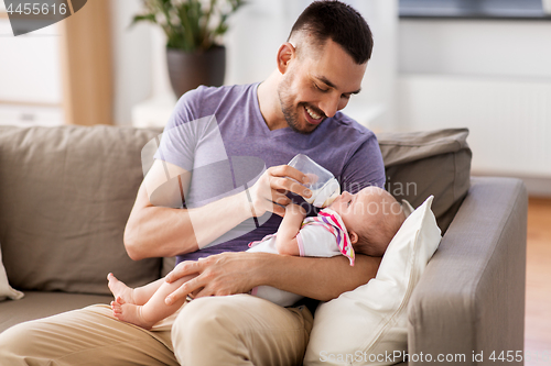 Image of father feeding baby daughter from bottle at home