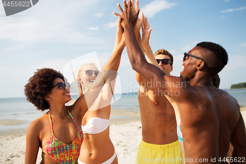 Image of happy friends making high five on summer beach