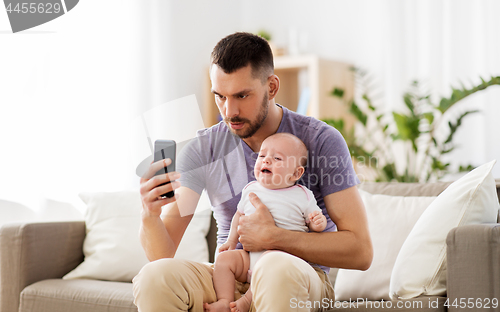 Image of father with crying baby and smartphone at home