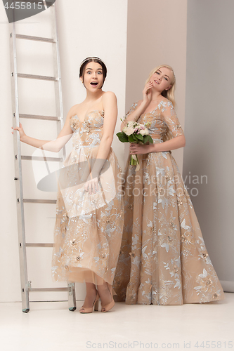 Image of Brides in beautiful dress standing indoors in white studio interior like at home. Trendy wedding style shot. Young attractive caucasian model like a bride tender looking.