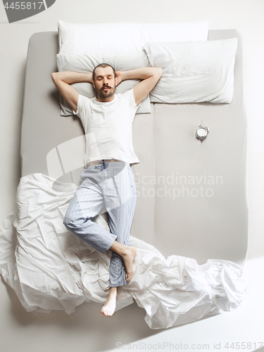 Image of Top view photo of young man sleeping in a big white bed