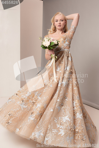 Image of Bride in beautiful dress standing indoors in white studio interior like at home. Trendy wedding style shot. Young attractive caucasian model like a bride tender looking.