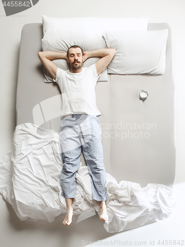 Image of Top view photo of young man sleeping in a big white bed