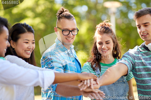 Image of happy smiling friends stacking hands in park