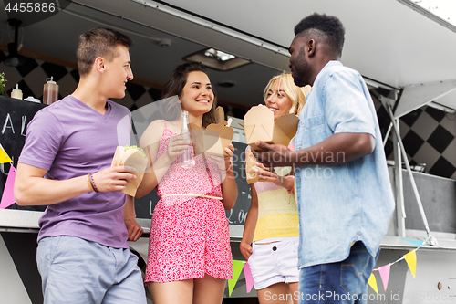 Image of happy friends with drinks eating at food truck