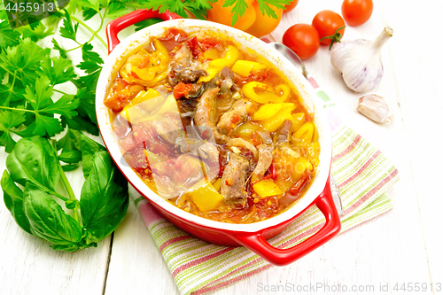 Image of Ragout of meat and vegetables in red brazier on light board