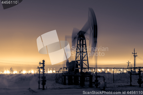 Image of Pump jack and refinery at night.