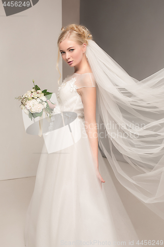 Image of Bride in beautiful dress standing indoors in white studio interior like at home. Trendy wedding style shot. Young attractive caucasian model like a bride tender looking.