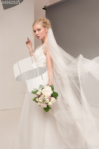 Image of Bride in beautiful dress standing indoors in white studio interior like at home. Trendy wedding style shot. Young attractive caucasian model like a bride tender looking.