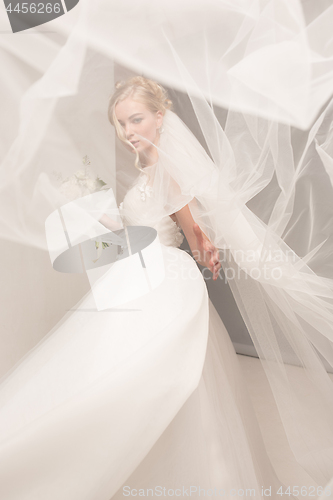 Image of Bride in beautiful dress standing indoors in white studio interior like at home. Trendy wedding style shot. Young attractive caucasian model like a bride tender looking.