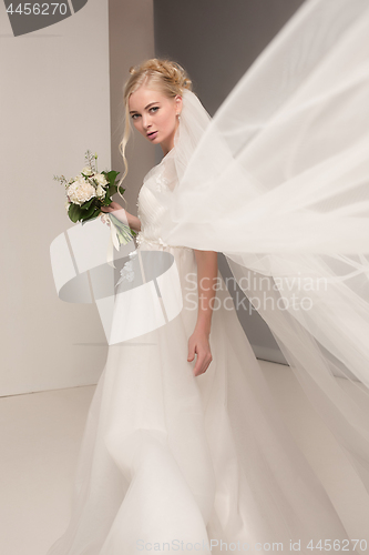 Image of Bride in beautiful dress standing indoors in white studio interior like at home. Trendy wedding style shot. Young attractive caucasian model like a bride tender looking.