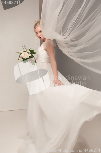 Image of Bride in beautiful dress standing indoors in white studio interior like at home. Trendy wedding style shot. Young attractive caucasian model like a bride tender looking.