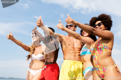 Image of happy friends showing thumbs up on summer beach