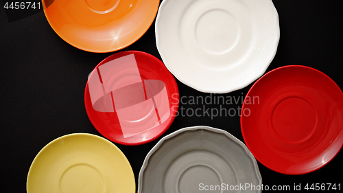 Image of Colorful empty plates and saucers over black background.