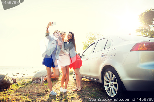 Image of happy women taking selfie near car at seaside