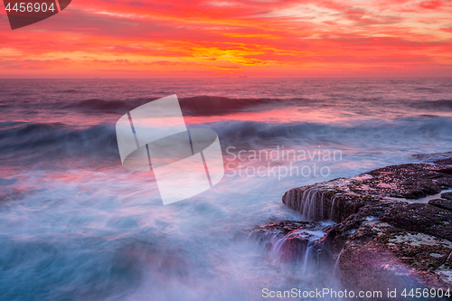 Image of Res skies over ocean as waves surge over rocks