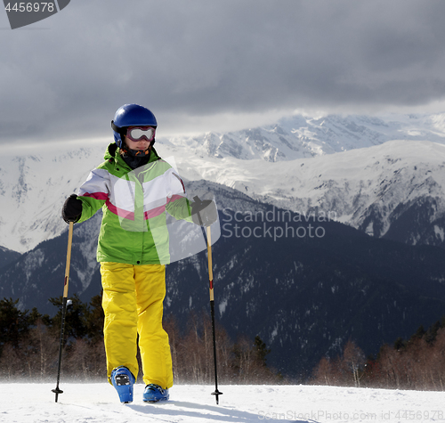 Image of Young skier with ski poles in sun mountains and gray sky before 