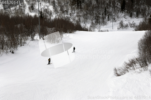 Image of Skier and snowboarder downhill on ski slope at gray winter day
