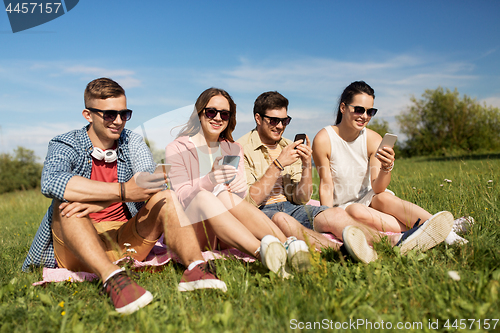 Image of smiling friends with smartphones sitting on grass