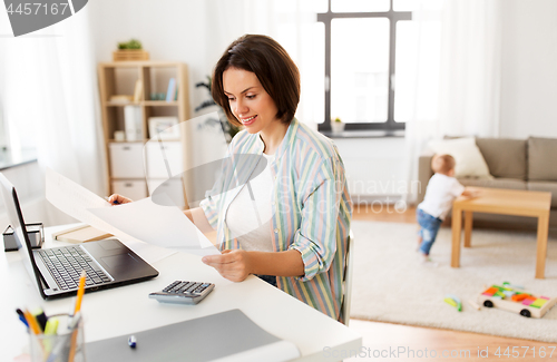 Image of mother working with papers and baby boy at home