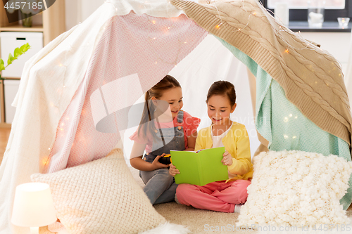 Image of little girls reading book in kids tent at home