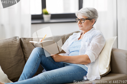 Image of senior woman writing to notebook or diary at home