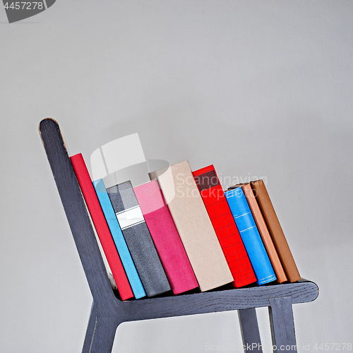 Image of Stack of colorful books on black wooden chair.