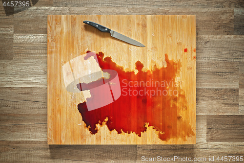 Image of Blood and knife on the big wooden cutting board.