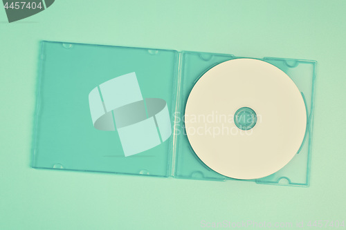 Image of White cd in transparent case on pastel green background.