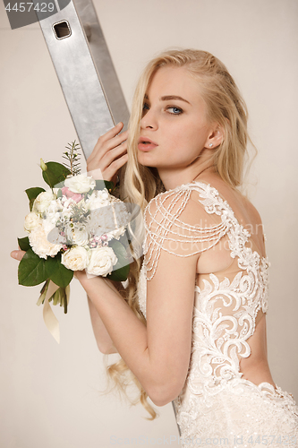 Image of Bride in beautiful dress standing indoors in white studio interior like at home. Trendy wedding style shot. Young attractive caucasian model like a bride tender looking.