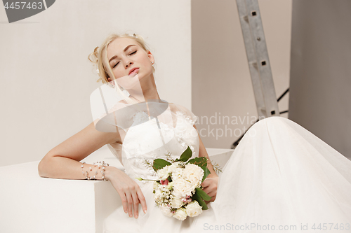 Image of Bride in beautiful dress standing indoors in white studio interior like at home. Trendy wedding style shot. Young attractive caucasian model like a bride tender looking.