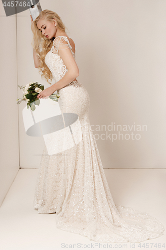 Image of Bride in beautiful dress standing indoors in white studio interior like at home. Trendy wedding style shot. Young attractive caucasian model like a bride tender looking.