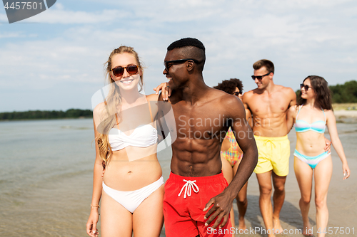 Image of mixed race couple walking along beach with friends