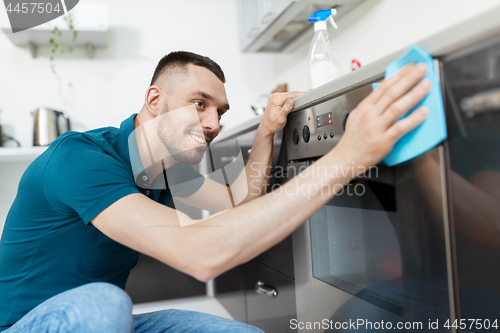 Image of man with rag cleaning oven door at home kitchen