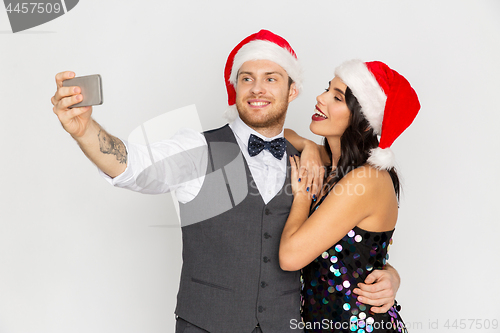 Image of couple in santa hats aking selfie at christmas