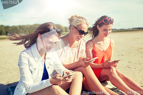 Image of group of happy women with smartphones on beach