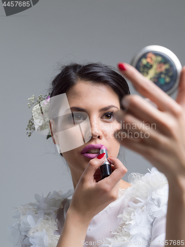 Image of bride paints lips with lipstick