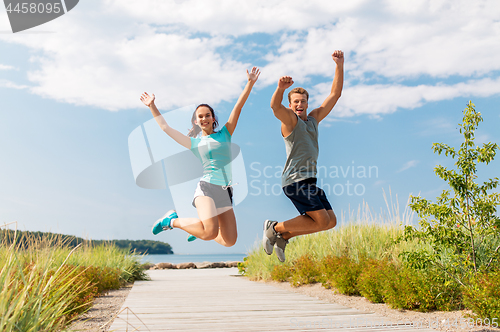 Image of happy couple in sports clothes jumping on beach