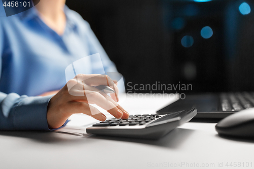 Image of businesswoman with calculator at night office