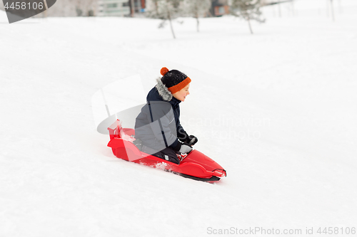 Image of happy boy sliding on sled down snow hill in winter