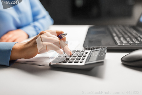 Image of businesswoman with calculator at night office