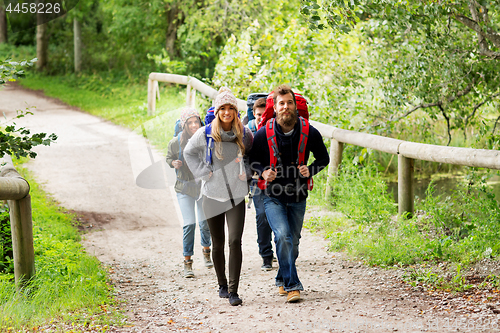 Image of happy friends or travelers hiking with backpacks