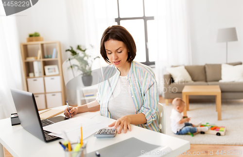 Image of mother working at laptop and baby boy at home