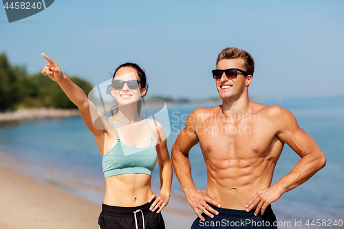 Image of happy couple in sports clothes and shades on beach