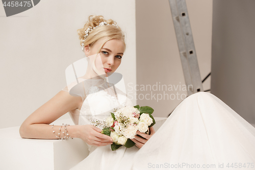 Image of Bride in beautiful dress standing indoors in white studio interior like at home. Trendy wedding style shot. Young attractive caucasian model like a bride tender looking.