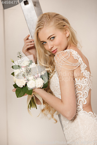 Image of Bride in beautiful dress standing indoors in white studio interior like at home. Trendy wedding style shot. Young attractive caucasian model like a bride tender looking.