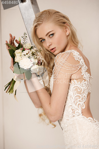 Image of Bride in beautiful dress standing indoors in white studio interior like at home. Trendy wedding style shot. Young attractive caucasian model like a bride tender looking.