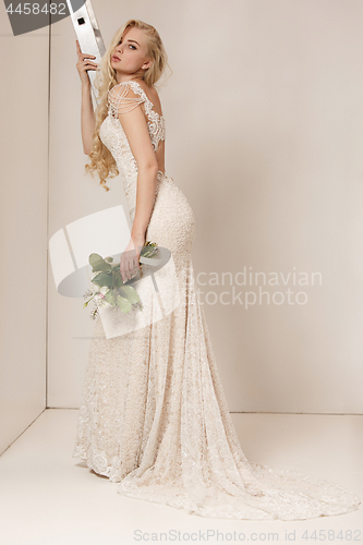 Image of Bride in beautiful dress standing indoors in white studio interior like at home. Trendy wedding style shot. Young attractive caucasian model like a bride tender looking.