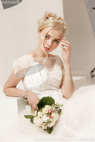 Image of Bride in beautiful dress standing indoors in white studio interior like at home. Trendy wedding style shot. Young attractive caucasian model like a bride tender looking.